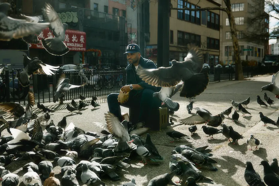 Urban portrait of Jason Roman surrounded by pigeons on a New York City sidewalk, capturing movement, street culture, and everyday life in a dynamic metropolitan environment.