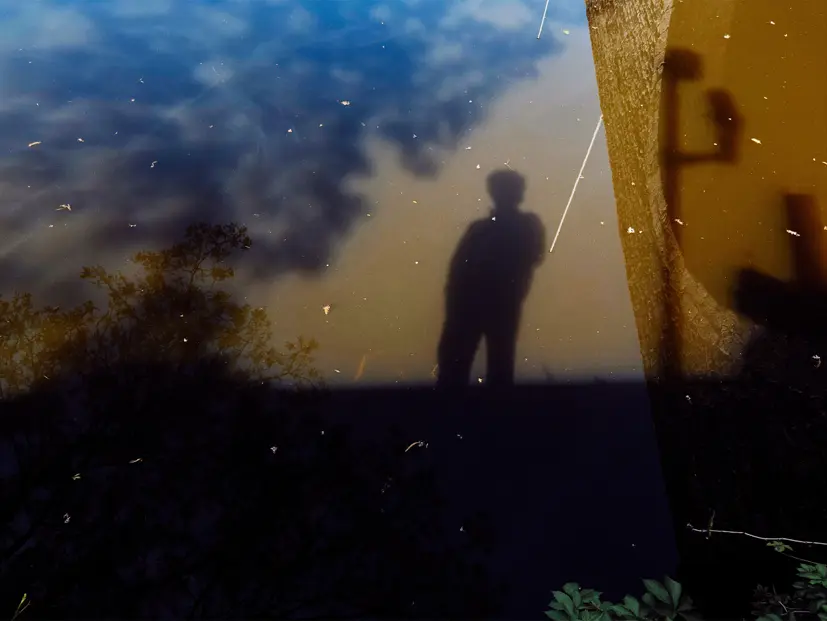 Silhouette reflected in still water alongside trees and sky, creating an abstract composition that blends nature, reflection, and visual storytelling.