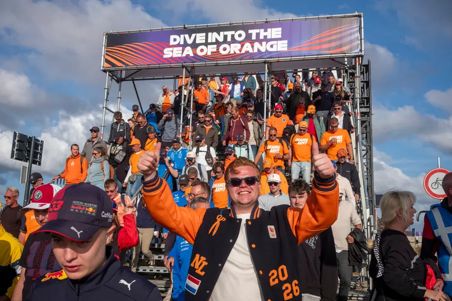 Formula 1 fans in orange descend a crowded grandstand at the Dutch Grand Prix in Zandvoort, beneath a “Dive into the Sea of Orange” banner.