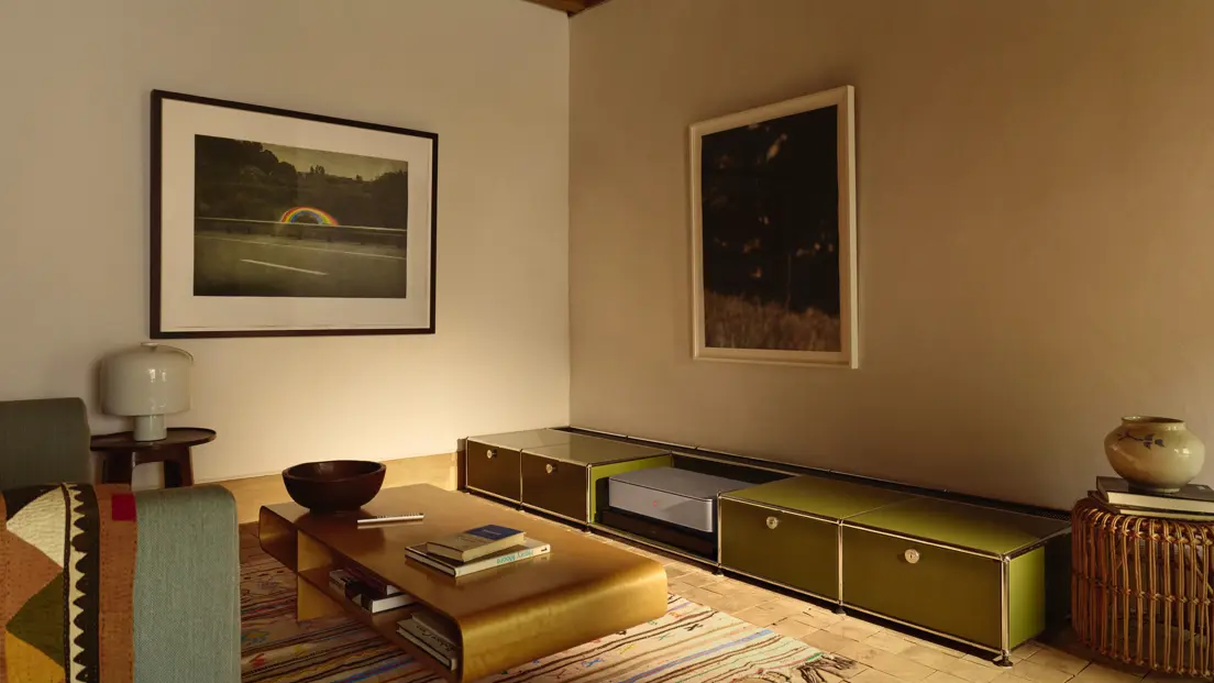 A warmly lit living room with framed photographs, a low wooden coffee table and modular storage furniture.
