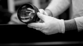 A person is holding a Leica lens while wearing gloves.