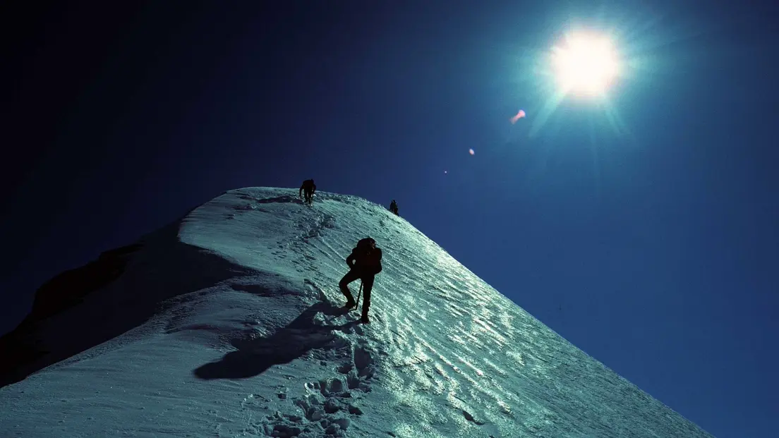 Three persons on the glacier in the dark, illuminated by the moon.