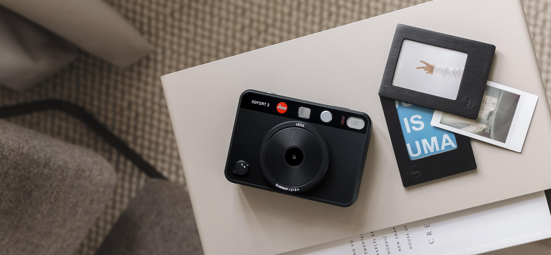 Three prints in frames next to the Leica Sofort 2 black. 