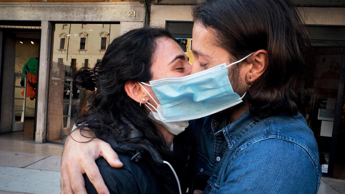 A couple wearing face masks hug and kiss in a street