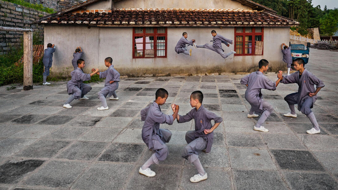 Shaolin monks practise martial arts in the courtyard in front of a traditional building