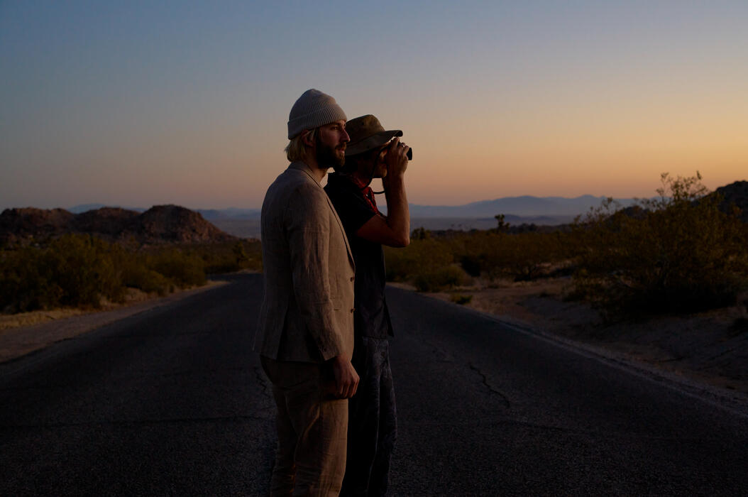 Garrett and Gantry Hill in a desert landscape at sunset, one looking through a camera.