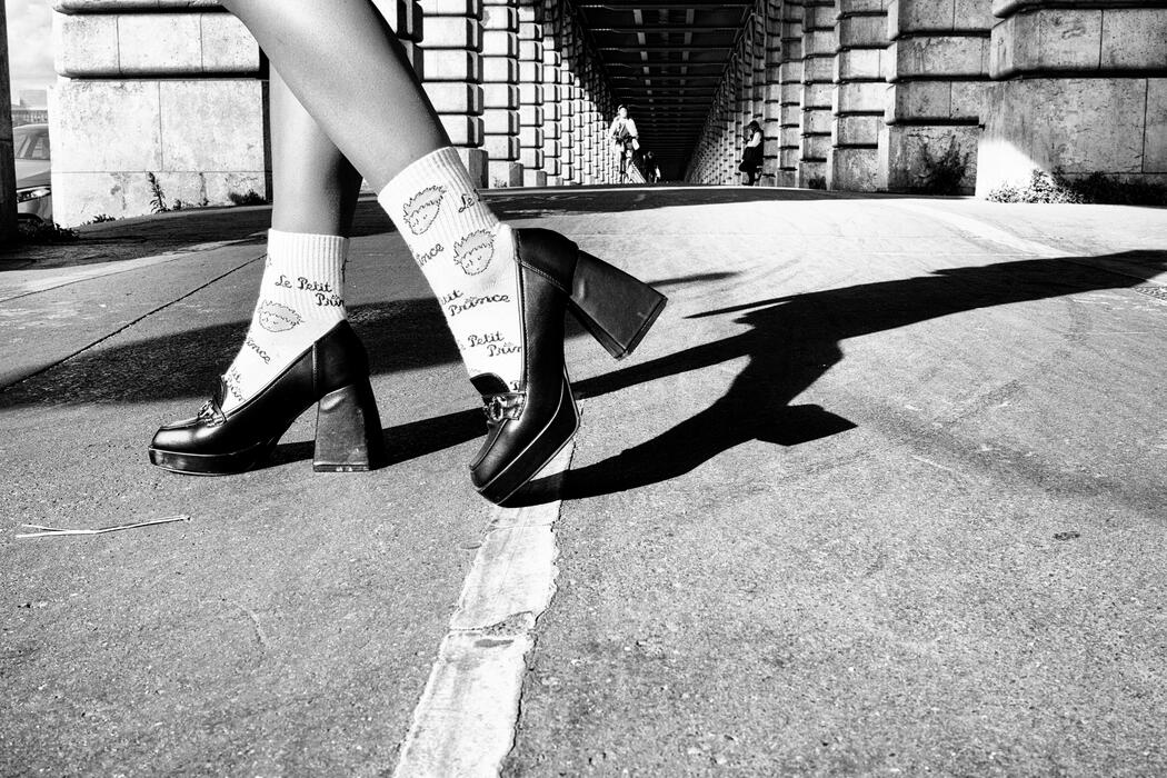 Close-up of legs in high heels on a street under a bridge in black and white.