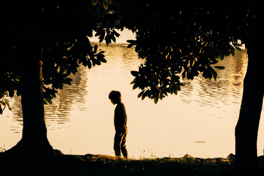 child between two trees in front of a sea