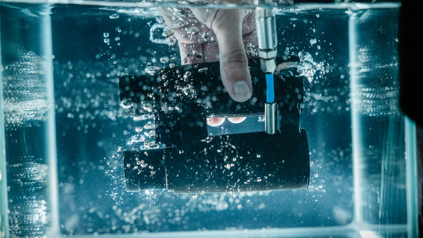 A worker dipping a pair of Leica binoculars under water