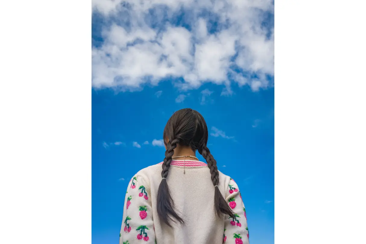 Woman with two plaits looks into the blue sky.