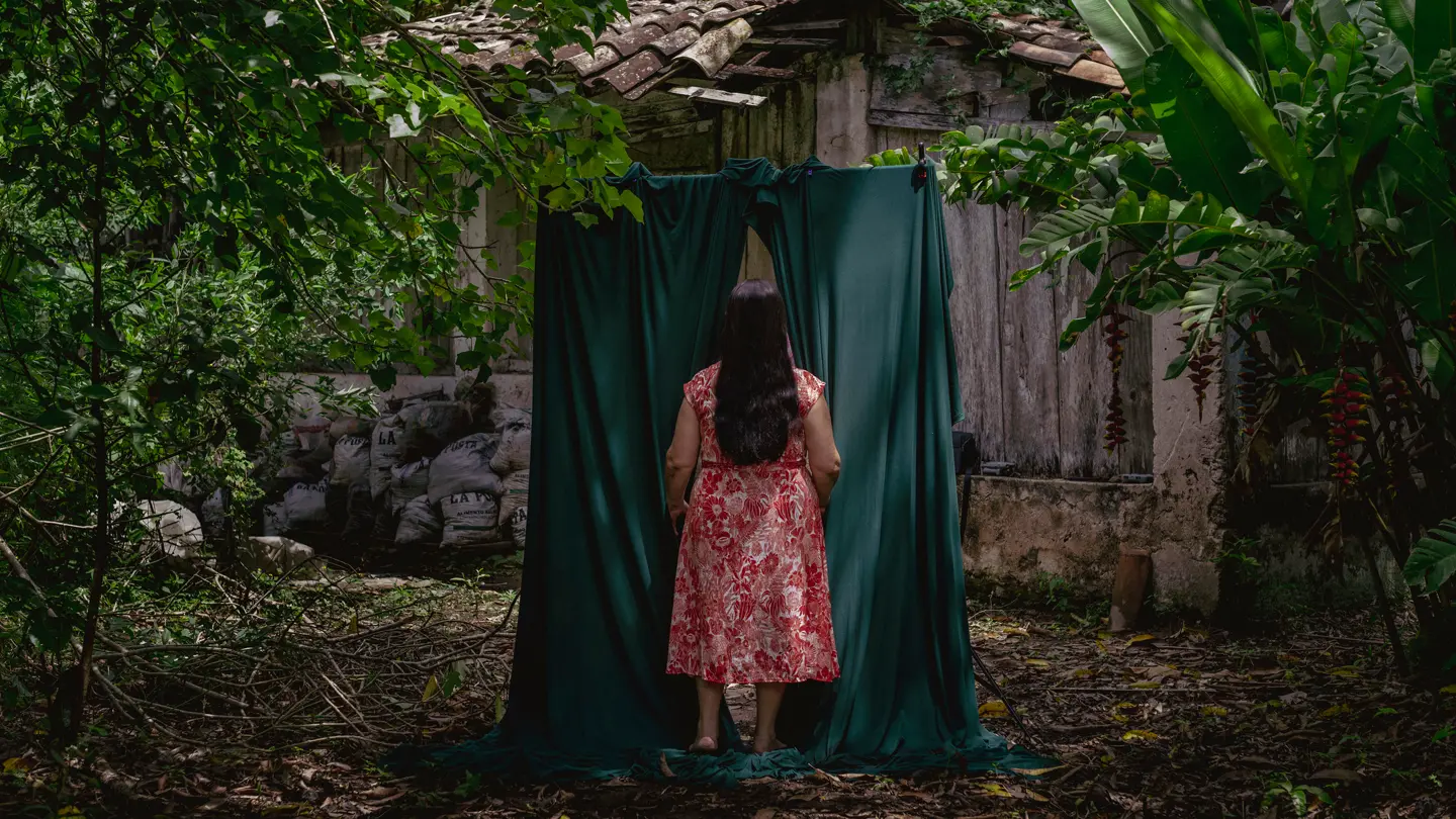 Woman in the forest walks through a green curtain behind a forest house