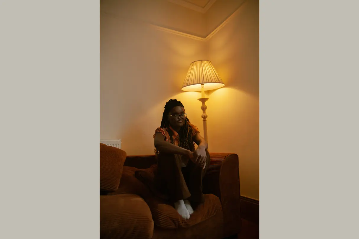 Colored girl sits with bent legs on a brown corduroy sofa