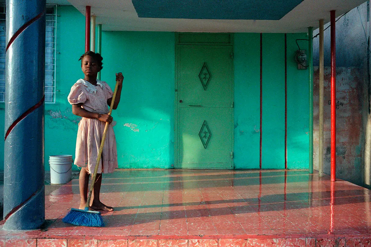 Coloured girl in a pink dress sweeping a floor