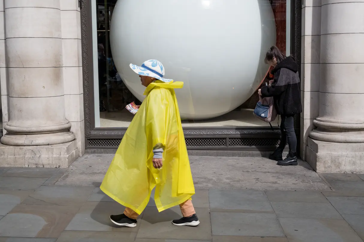 Woman wearing a yellow rain cape and a large hat on the pavement