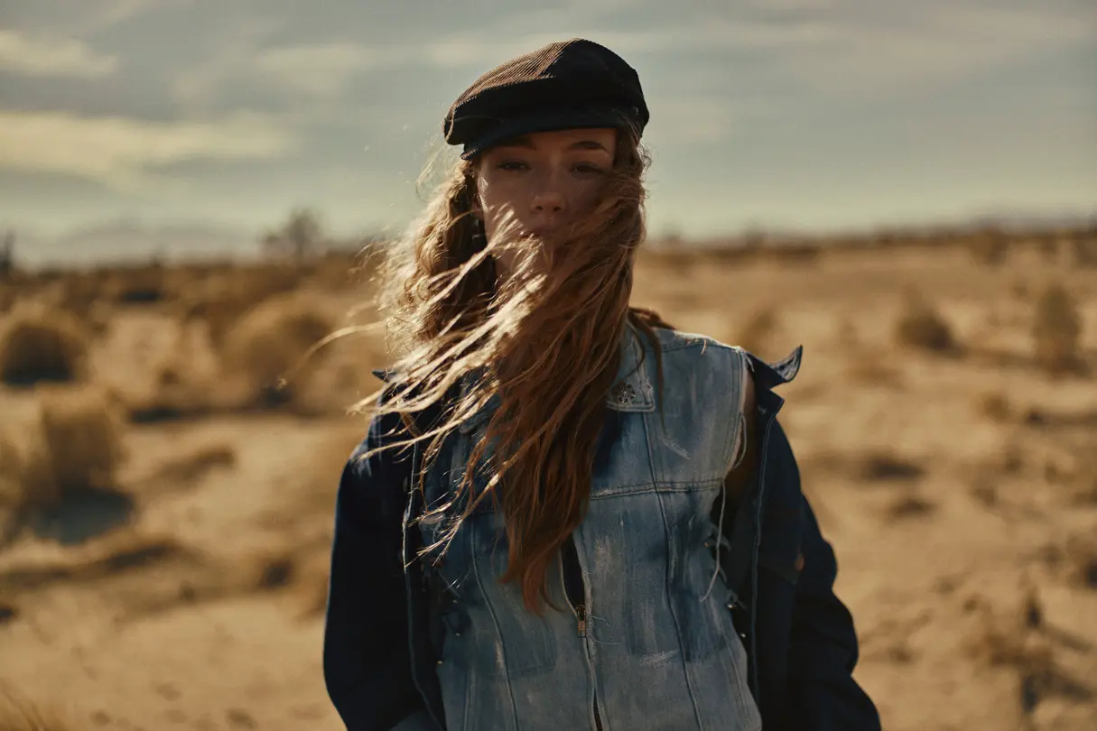 Portrait of a woman with a cap standing in the dessert with waving hair
