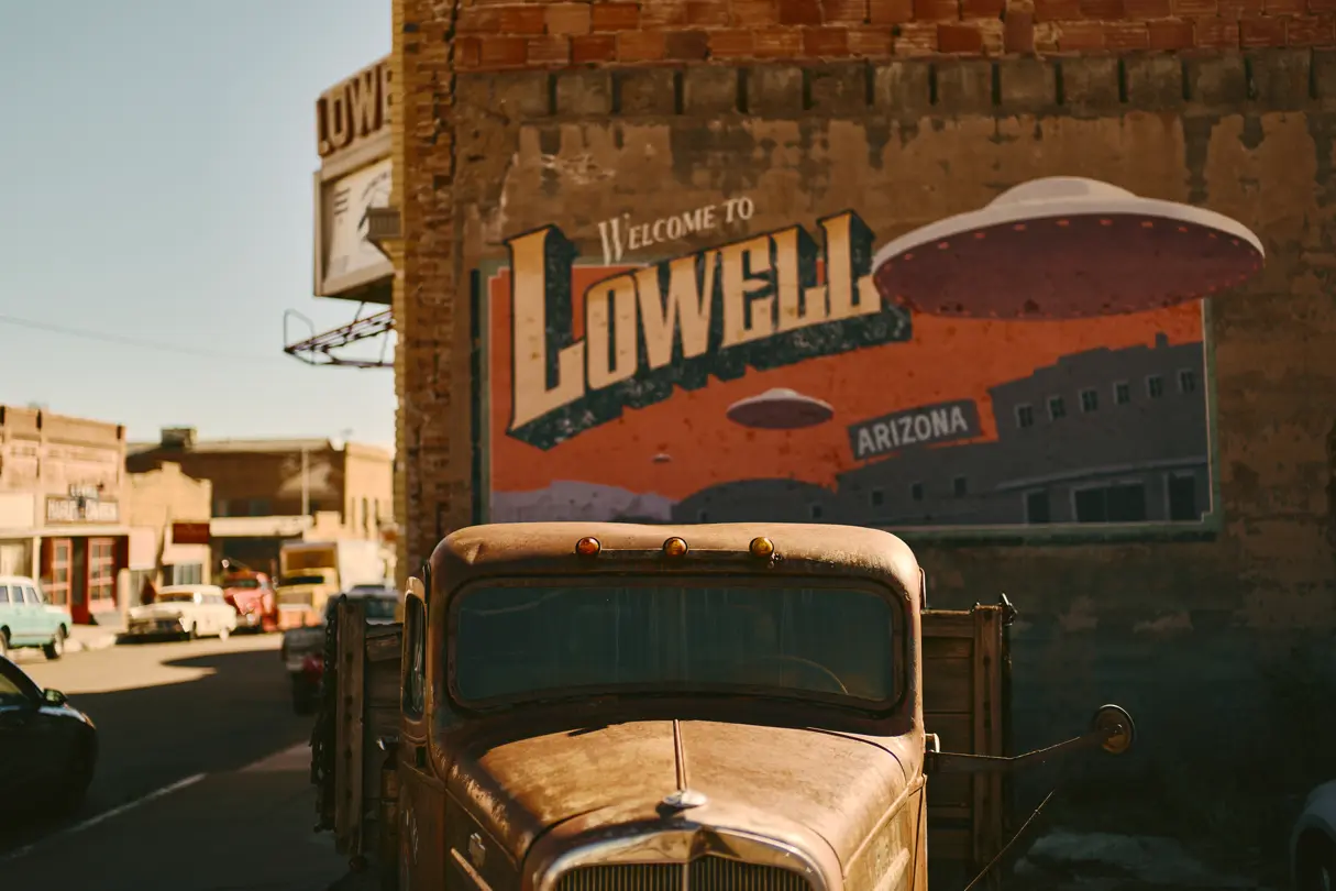 Old car in front of a house wall with the words ‘Welcome to Lowell, Arizona’