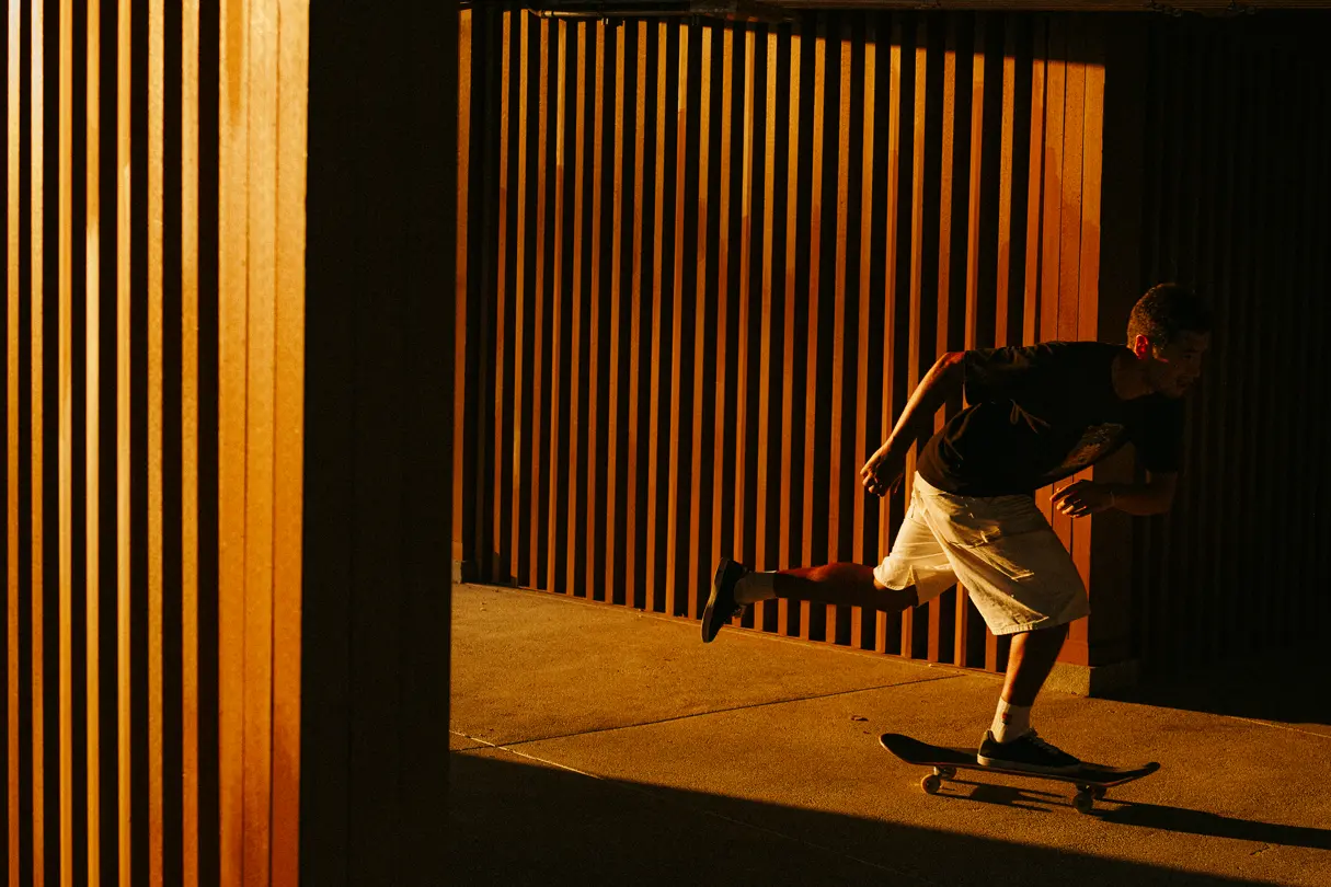 Person skateboarding past a wooden wall in warm evening light