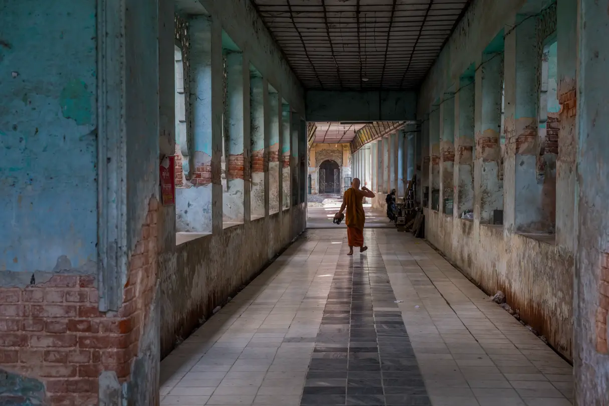 A monk with an orange robe walks alone down a corridor
