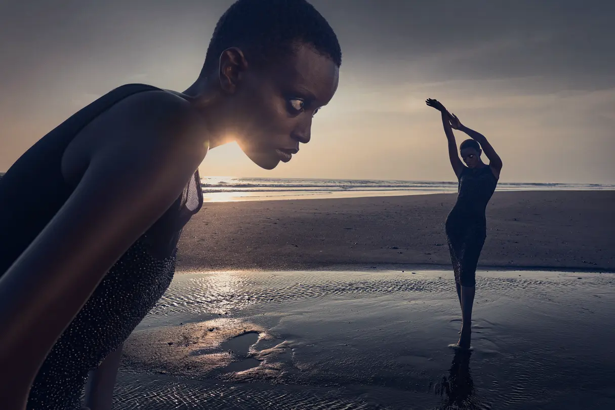 Two dark-skinned models with short hair are posing on the beach at sunset