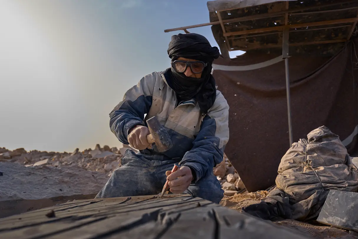 A hooded man in the desert with a hammer and chisel 