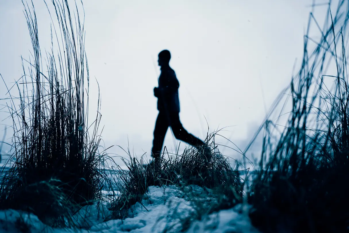 A man jogging in the background against a backdrop of seaweed covered in snow on the beach