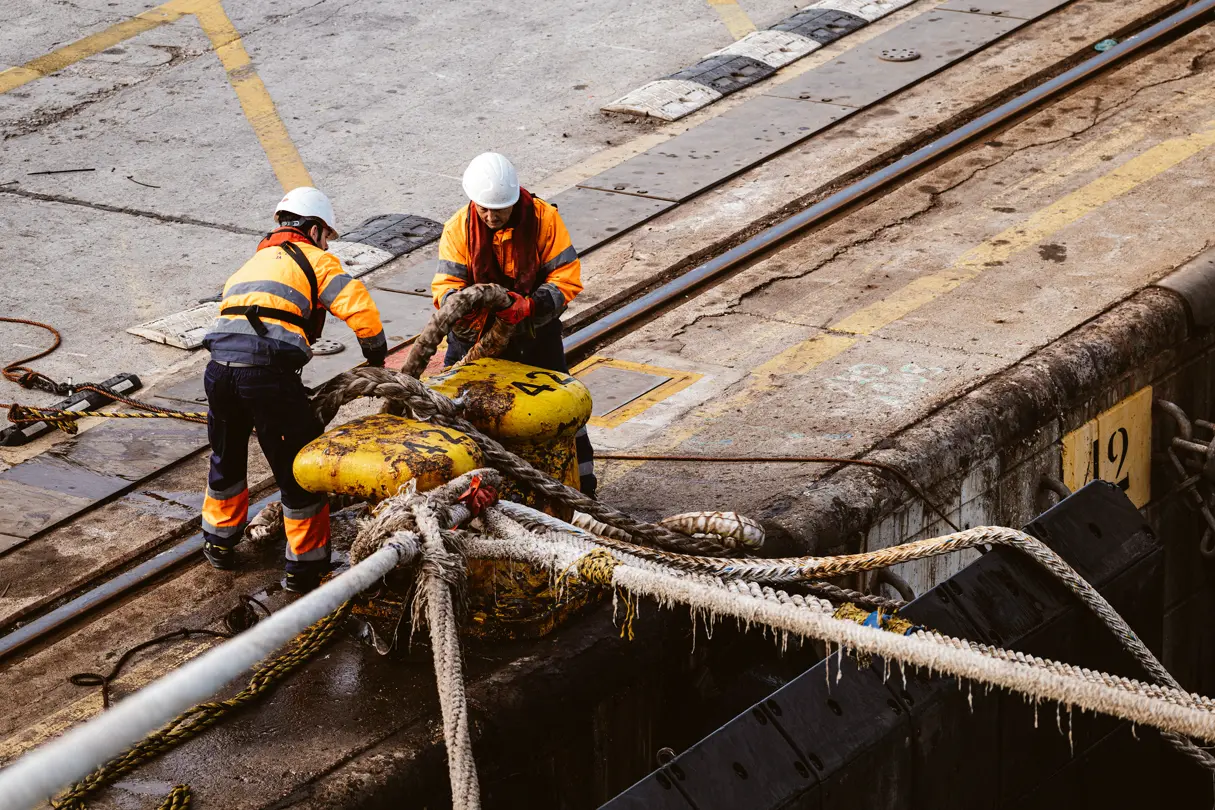 Two workers are securing a ship's rope to the jetty