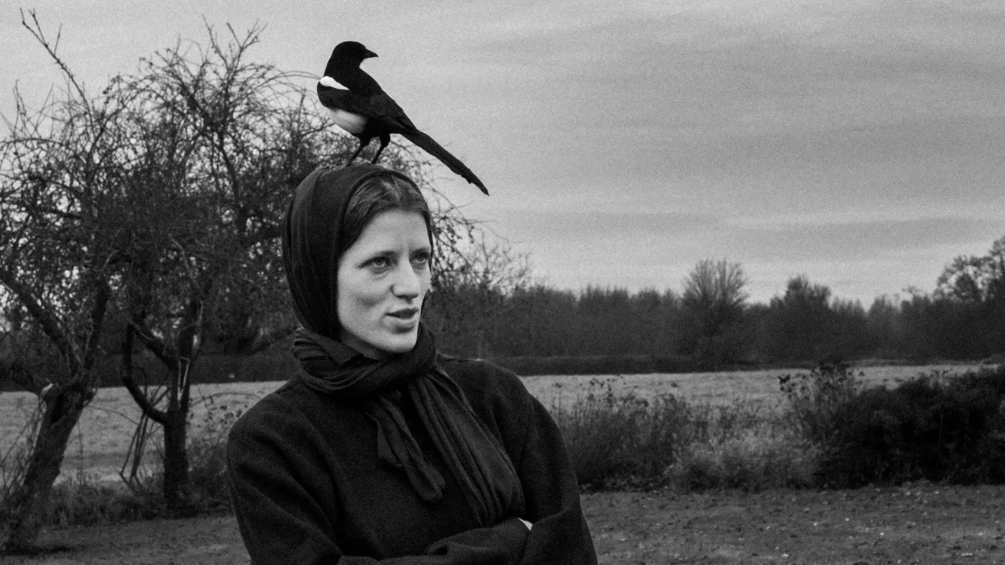 Black and white photo of a lady with a magpie bird on her head