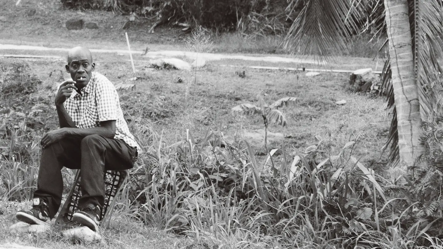 Black and White photo of a man sitting on a crate while smoking