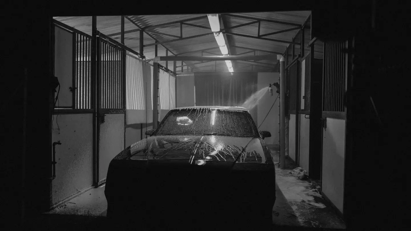 Black and white photograph of a car inside a car wash being cleaned