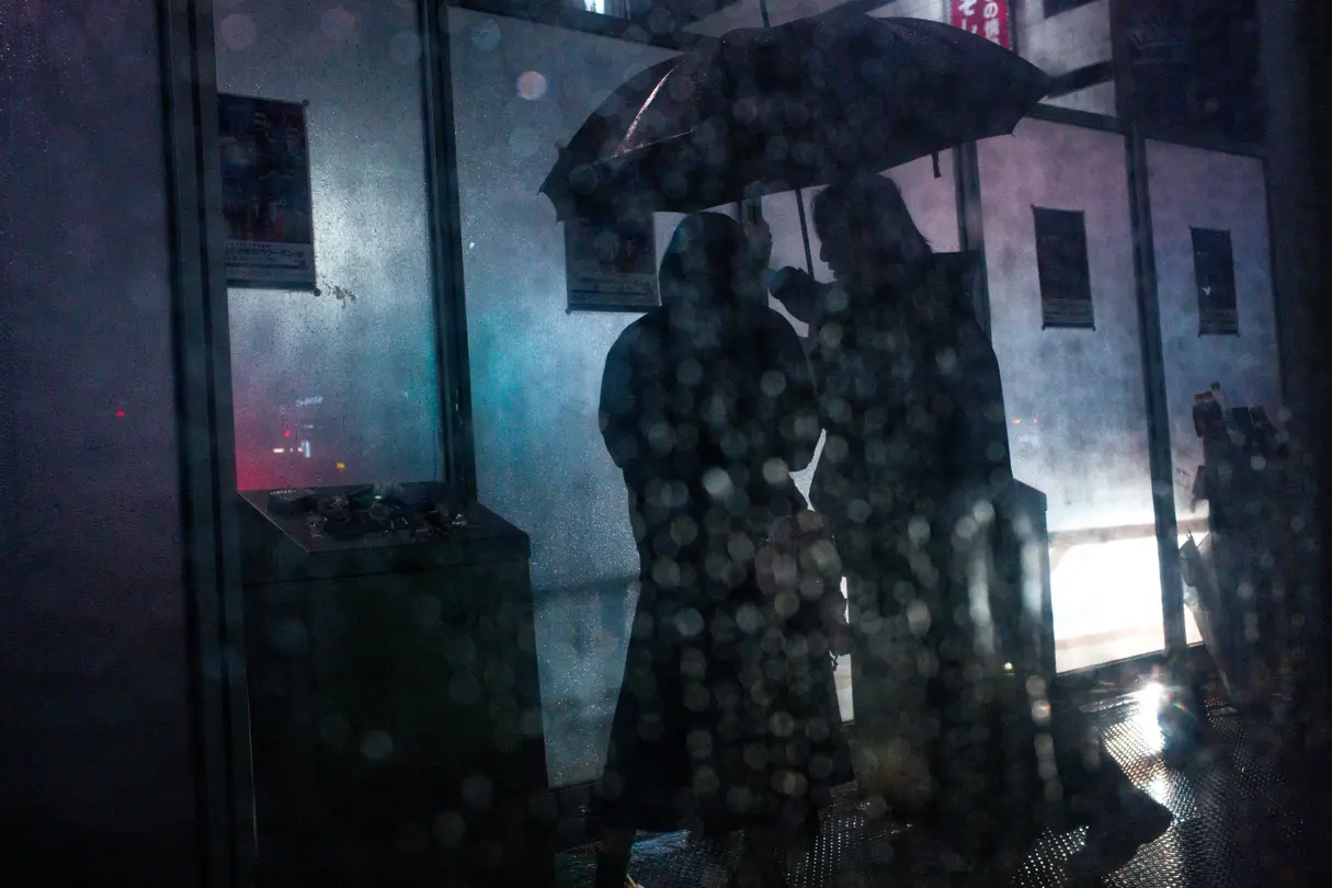 Two people are out for a walk in Tokyo in the evening in the rain, carrying umbrellas
