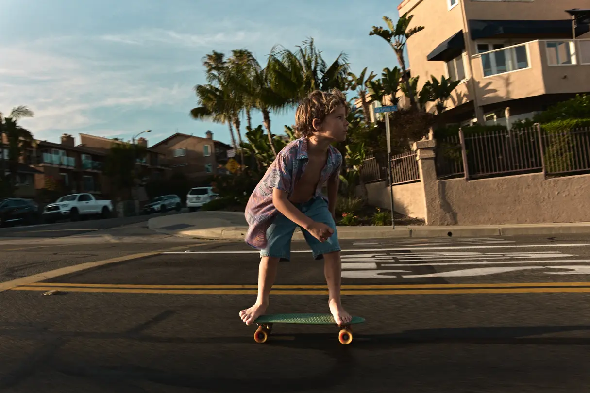 A boy is riding his skateboard barefoot along the street