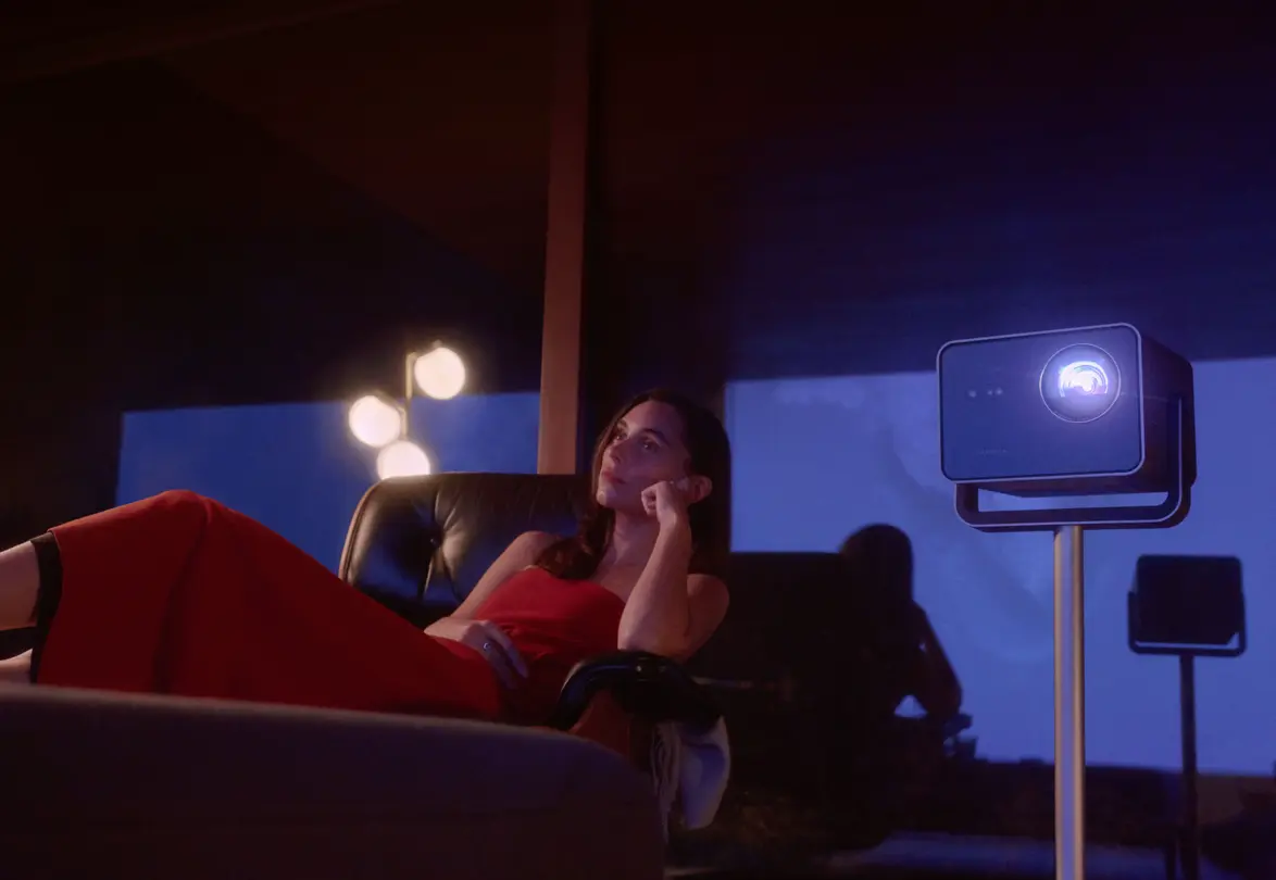 A woman is sitting in the living room watching the projection from the Leica Cine Play 1