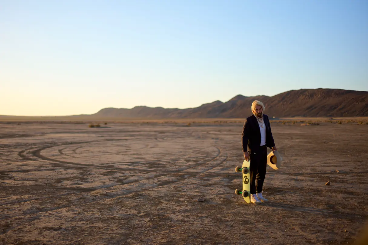 Man with long blonde hair with his skateboard in the dessert