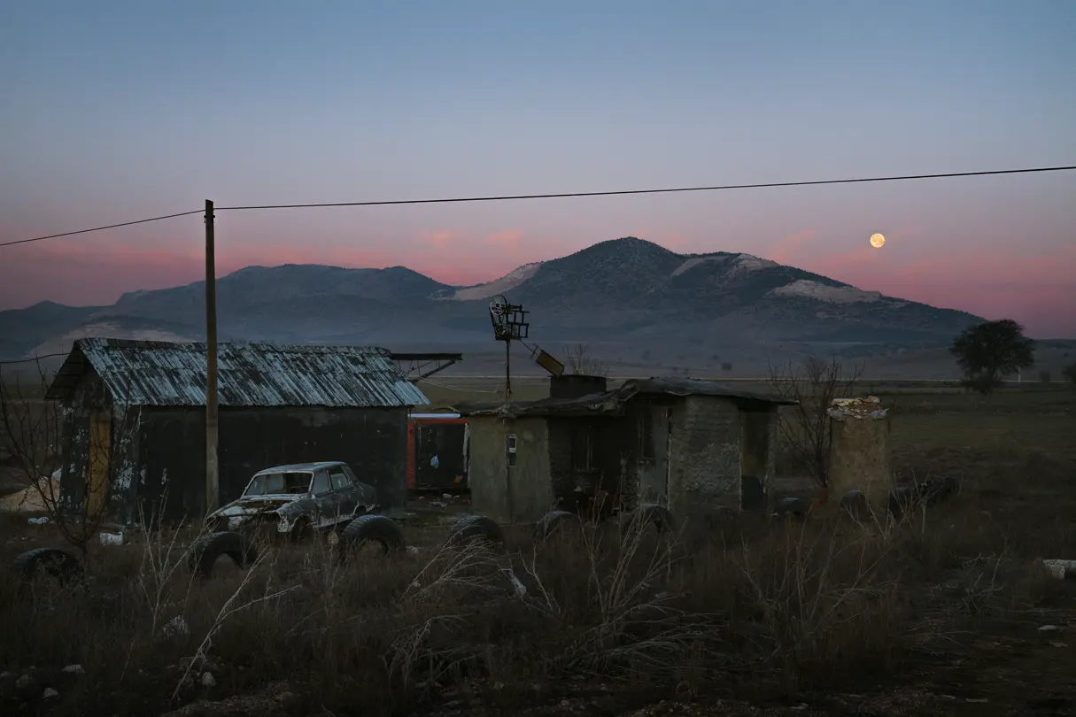 Two abandoned and dilapidated huts in the middle of nowhere, set against a mountain range at sunset