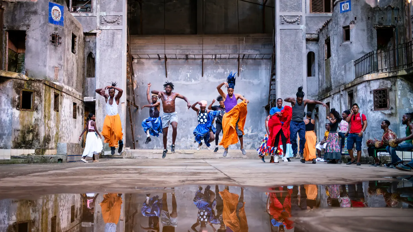 Traditional dancers performing in a historic courtyard in Cuba, captured mid-jump with vibrant costumes and reflections in a rain puddle.