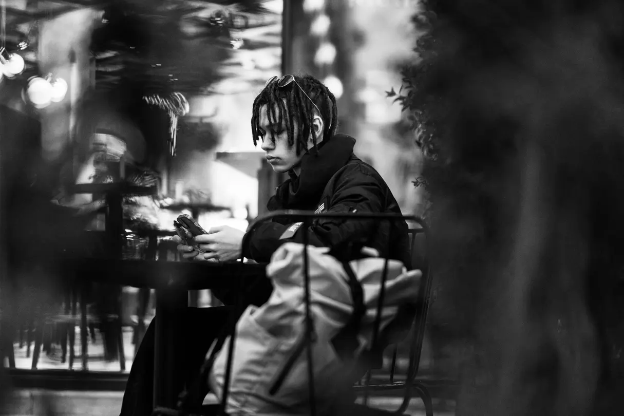 Young man with braids on a chair looking into his smartphone