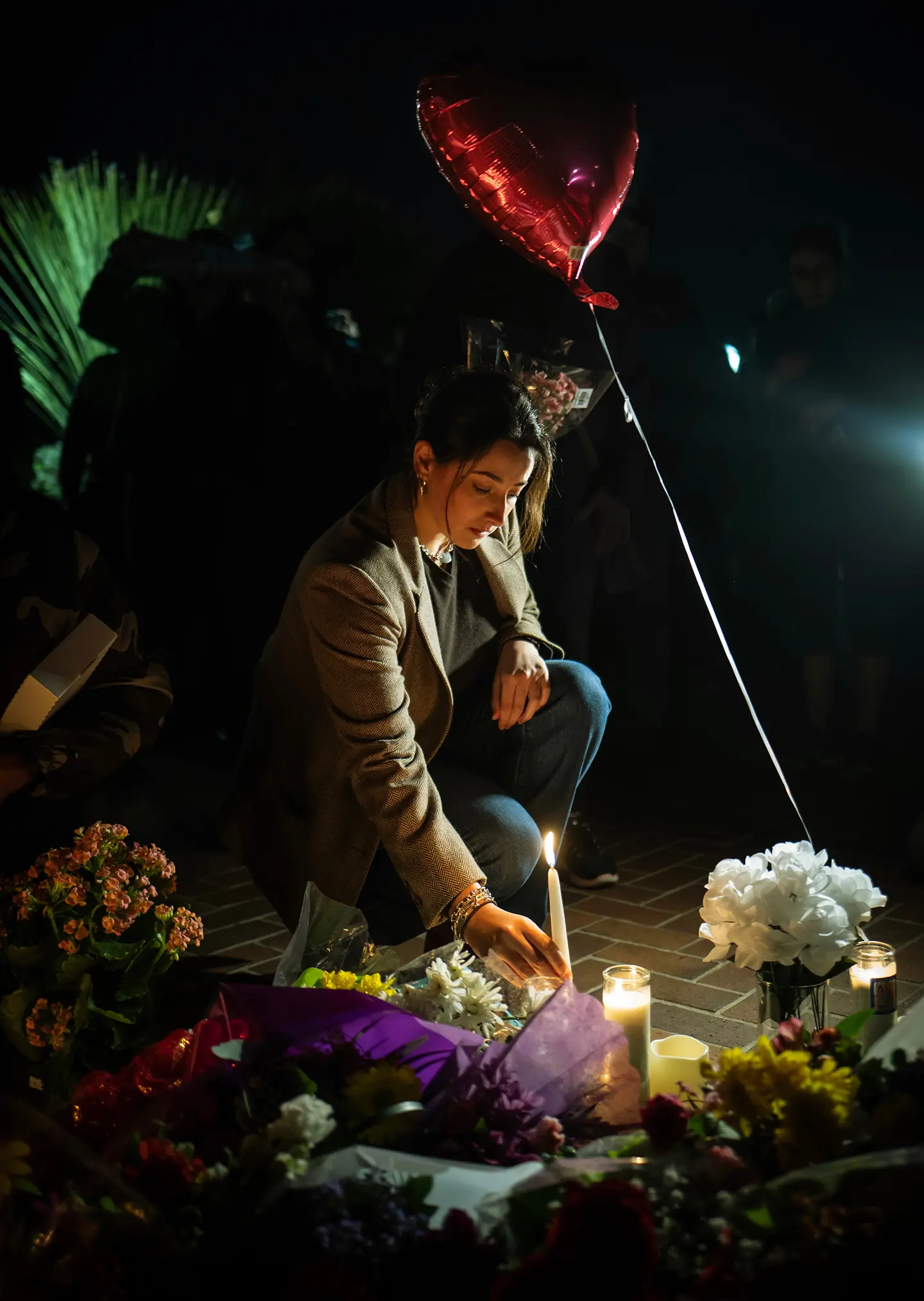 Woman placing flowers and candles at a memorial vigil, capturing remembrance, grief, and community support.