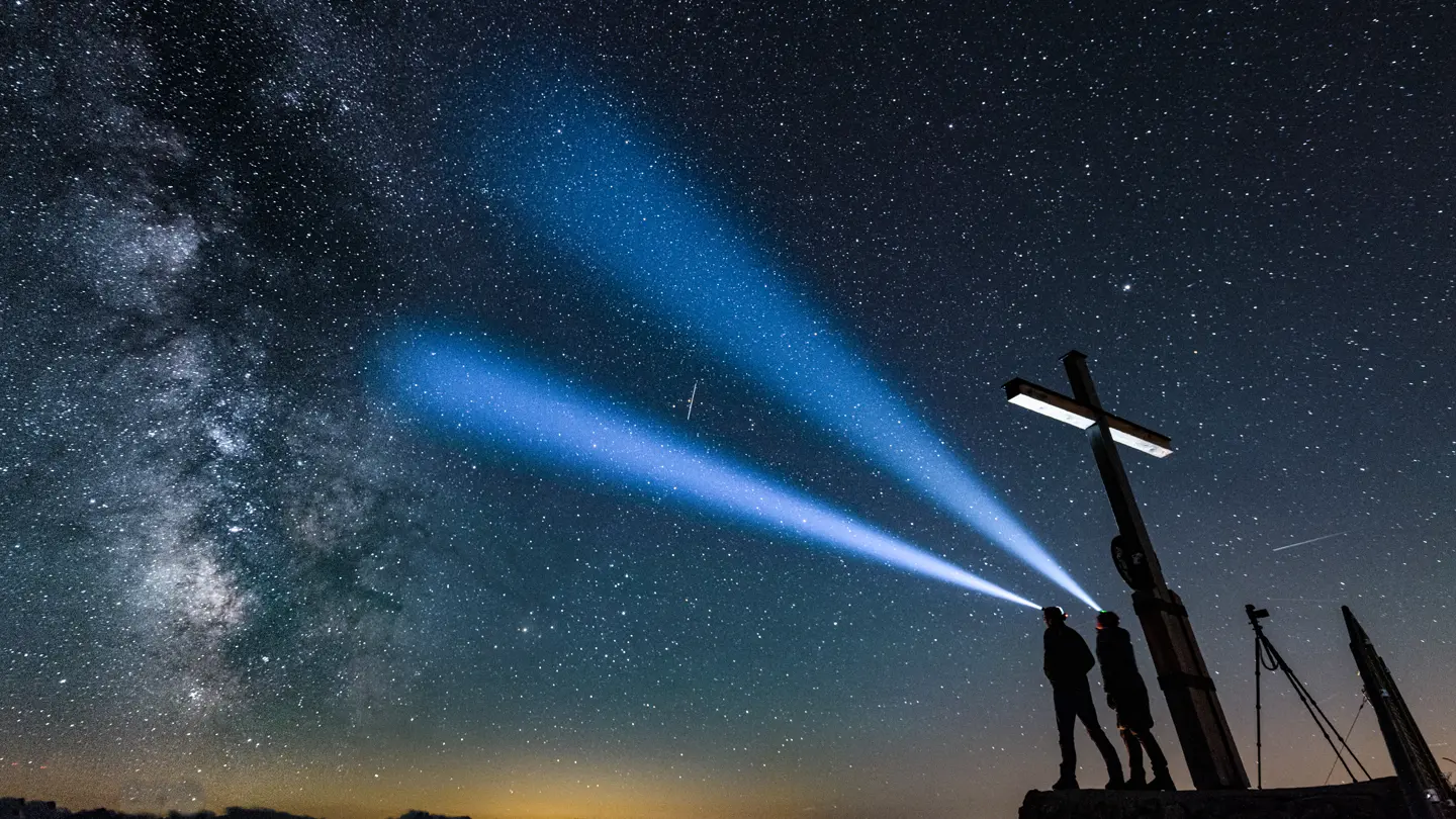 Two people shining headlamps beneath a star-filled night sky and the Milky Way.