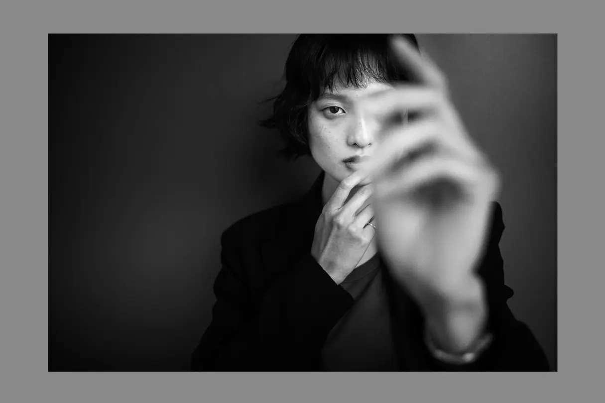 Black-and-white portrait of a young woman partially obscured by a raised hand. Minimalist street-inspired photography exploring identity, expression, and human connection.