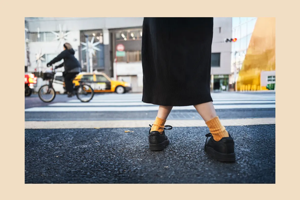 Pedestrian crossing a Tokyo street with warm-toned socks and city traffic in the background. Everyday urban photography highlighting movement, style, and contemporary city life.