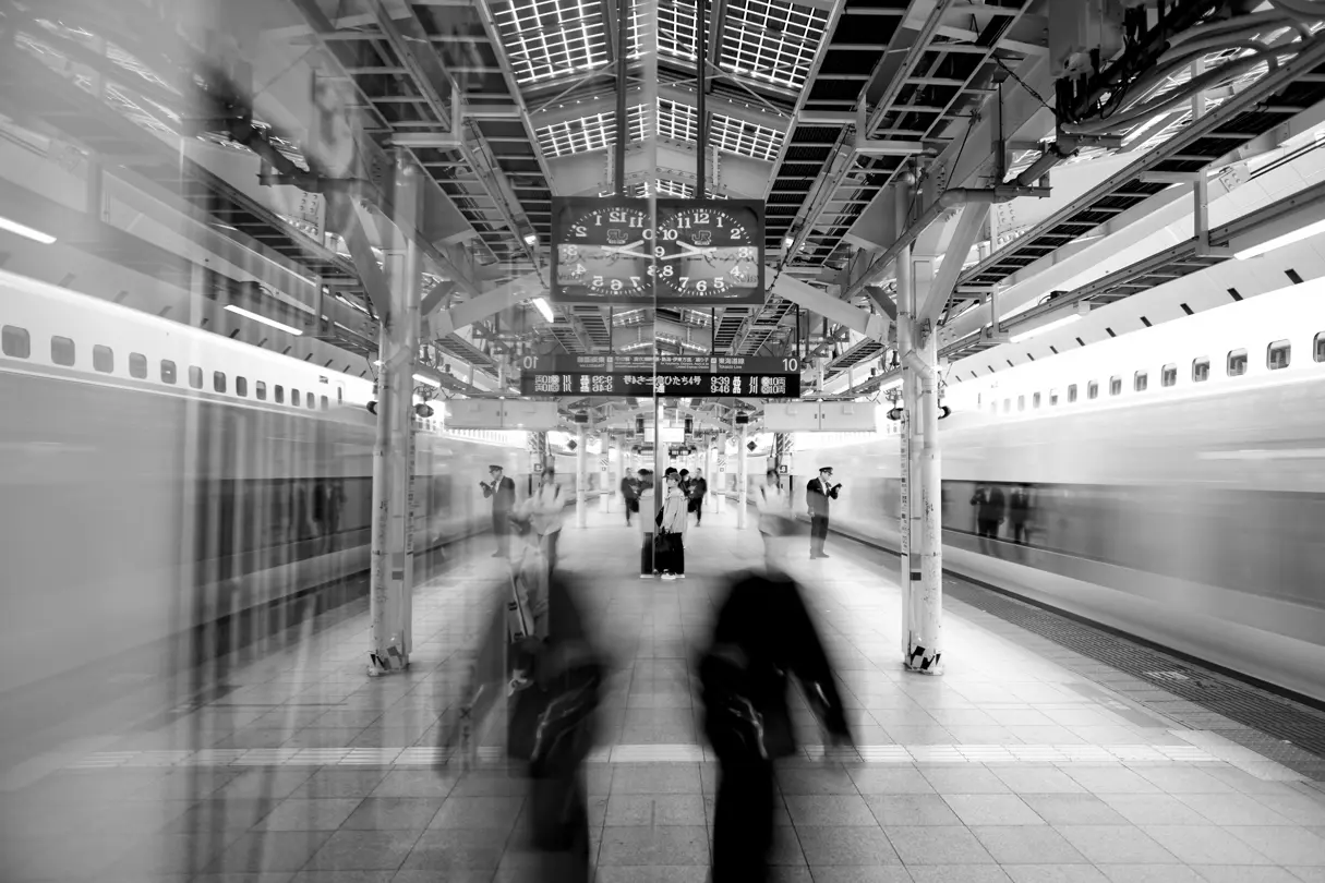 Shinkansen trains arrive at a busy Tokyo station, captured with motion blur and architectural symmetry.