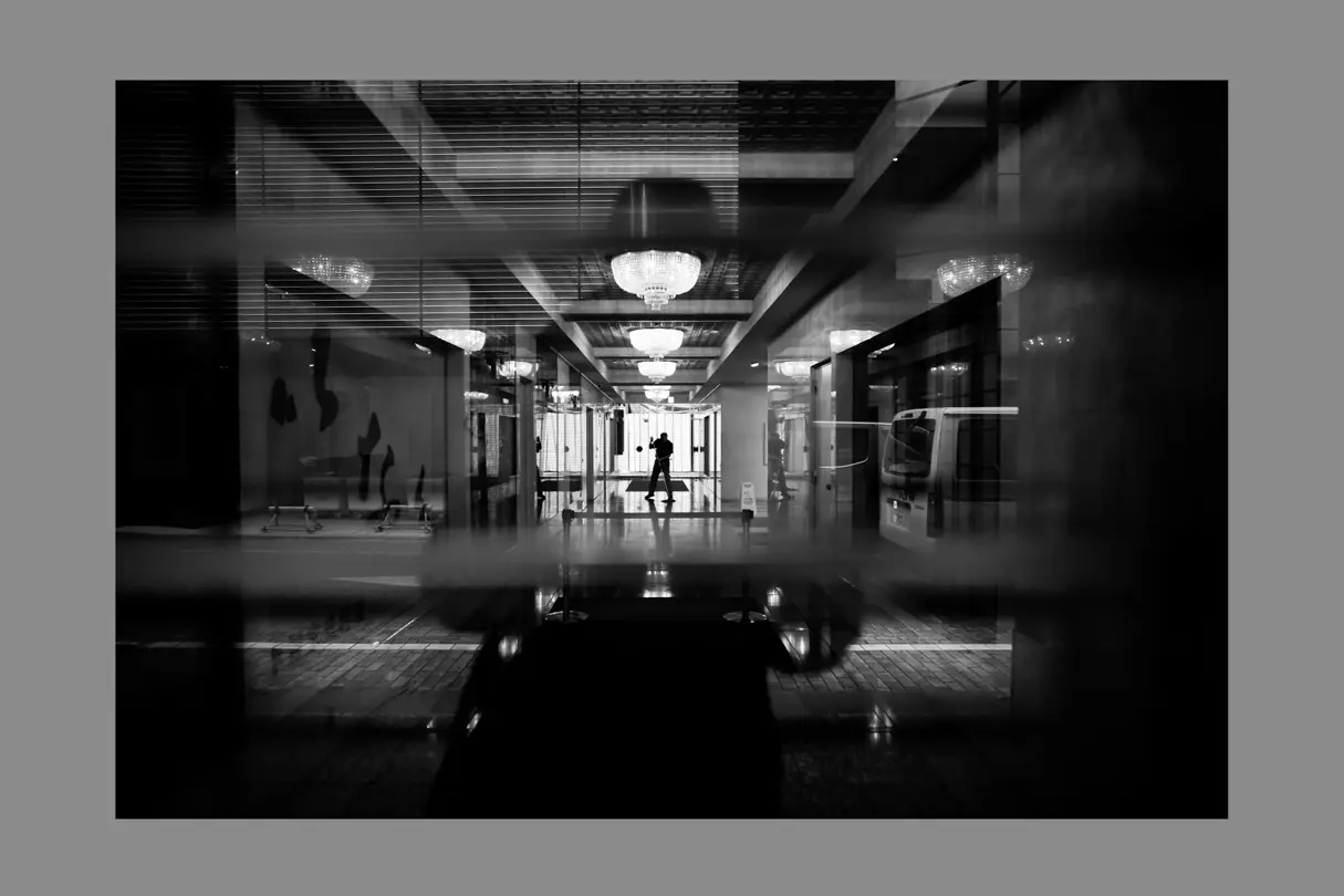 Modern Tokyo hotel lobby with reflections, chandeliers, and a silhouetted figure in black and white.