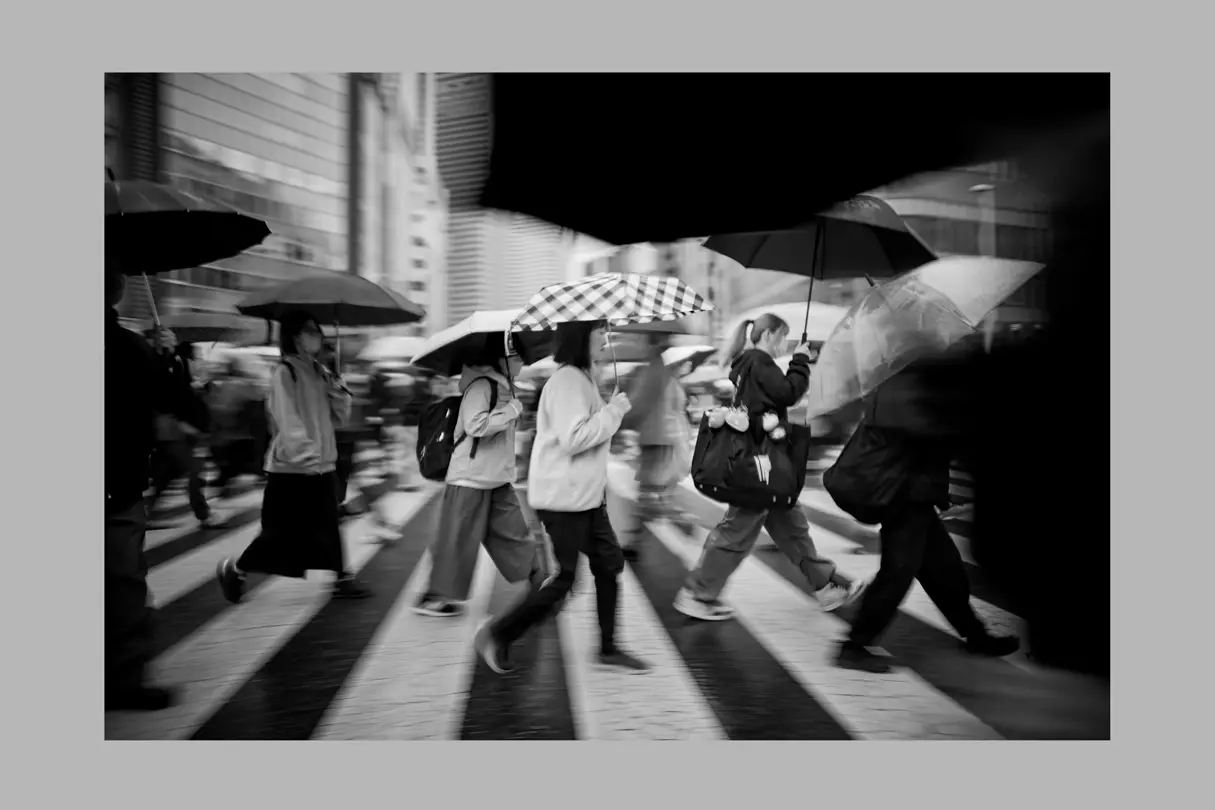 Pedestrians carrying umbrellas cross a busy Tokyo intersection on a rainy day.