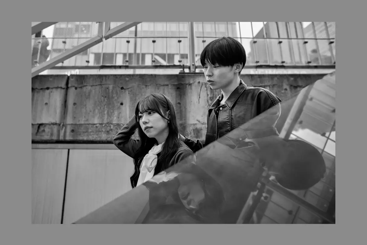 Two young people framed by modern Tokyo architecture with reflective surfaces and urban surroundings.