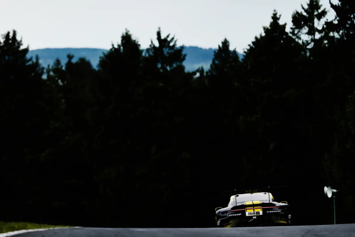 Race car disappearing into the distance on a forest-lined circuit, highlighting speed and endurance racing atmosphere.
