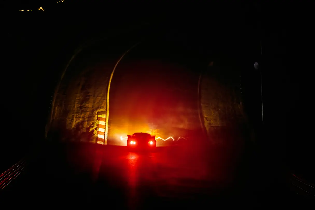 Race car illuminated by glowing taillights on a dark circuit, capturing the drama of nighttime endurance racing.