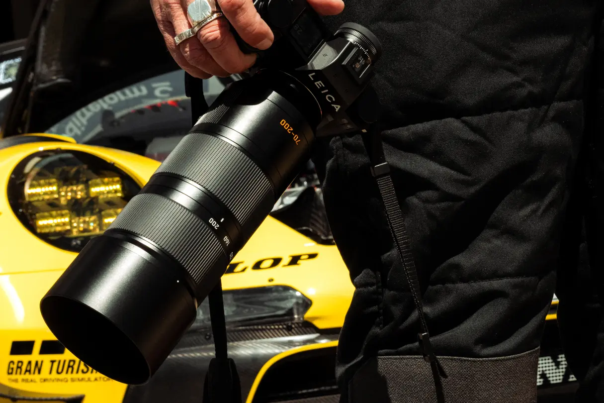 Leica SL3-P with telephoto lens positioned beside a GT race car, highlighting professional motorsport photography equipment.