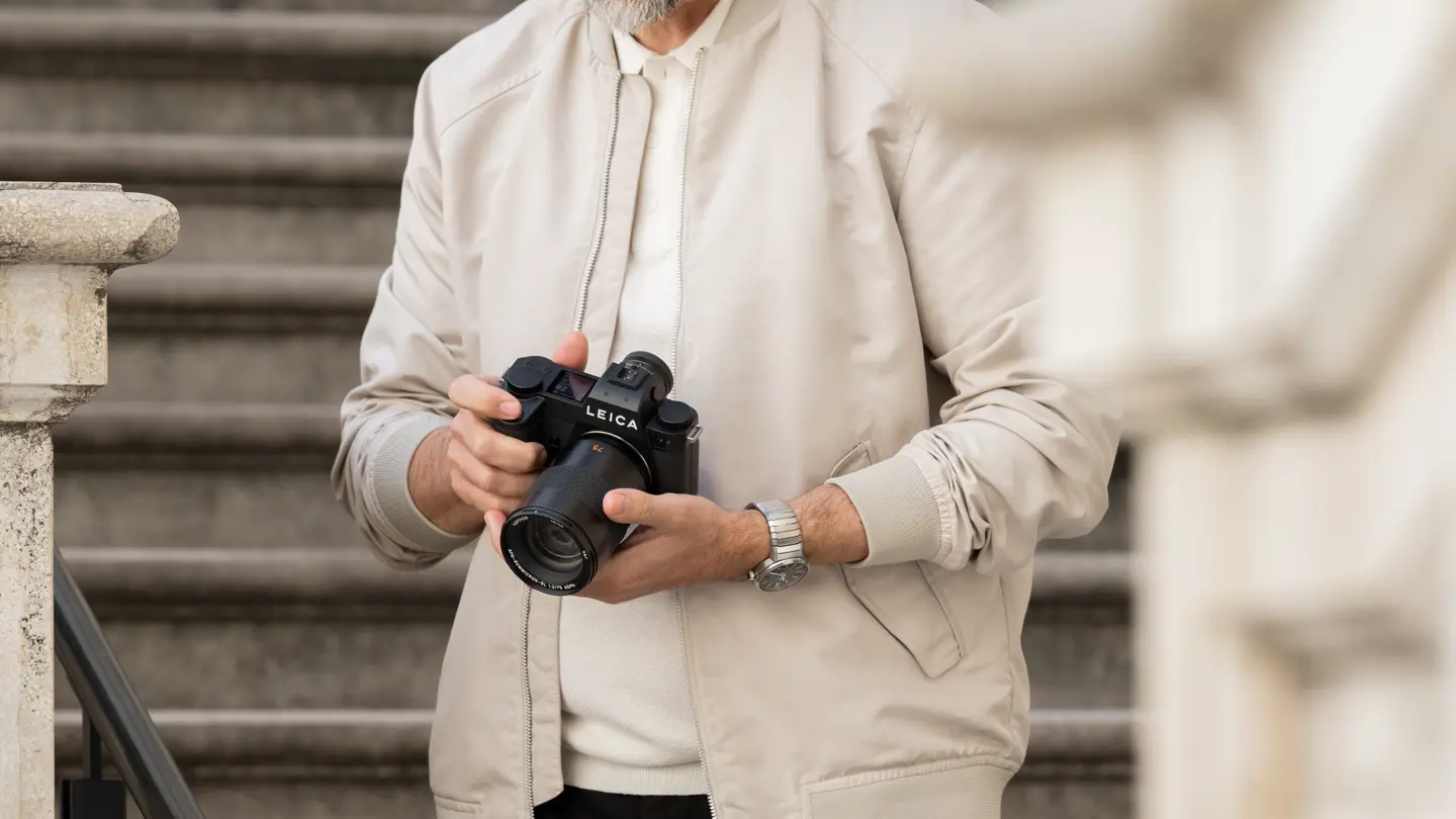 Photographer adjusting a Leica camera near an urban staircase.