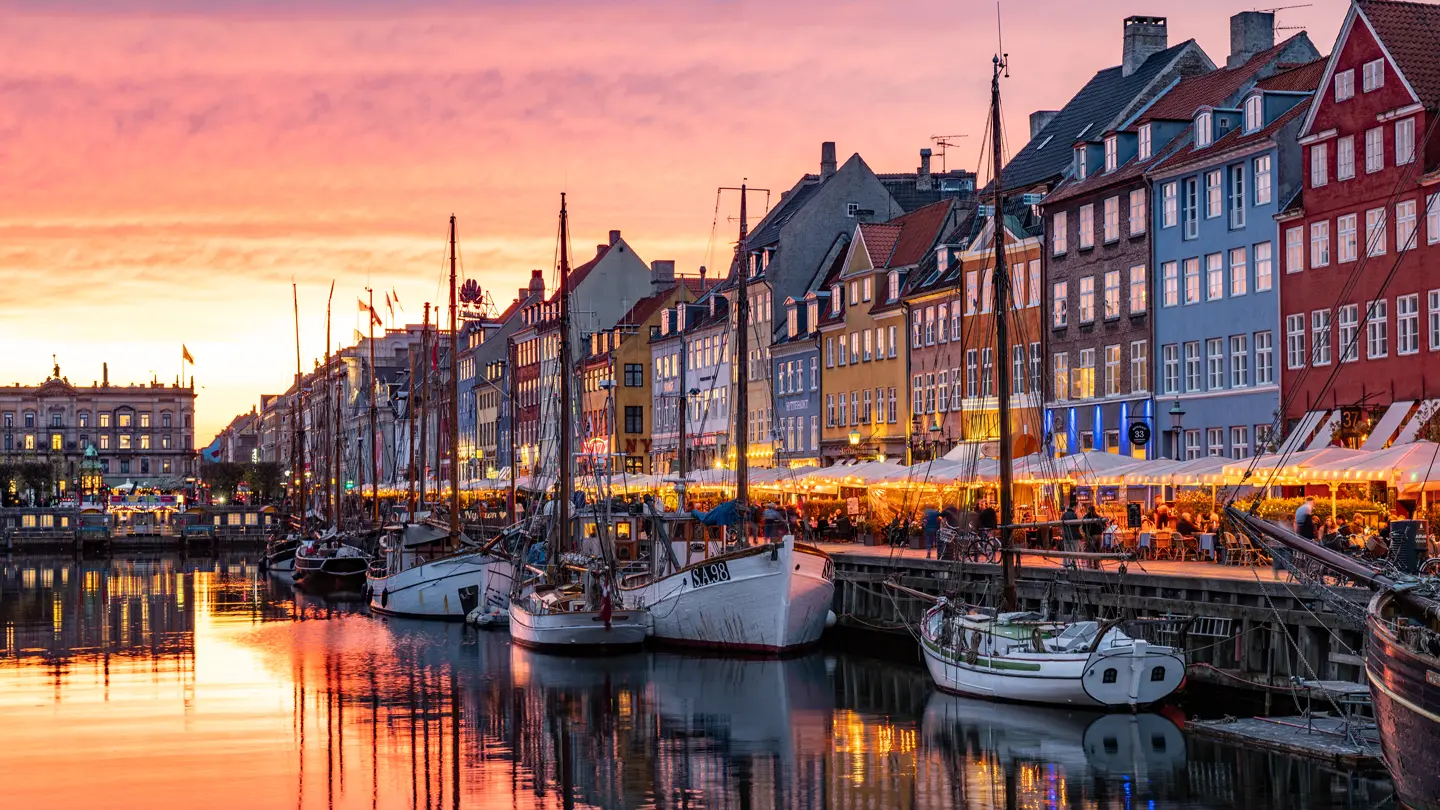 Colorful waterfront and historic buildings reflected in a harbor at sunset.