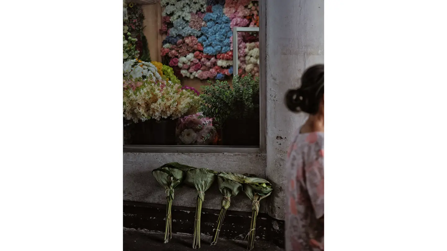 La vitrine d'un fleuriste, devant laquelle passe une femme vêtue d'un chemisier à fleurs